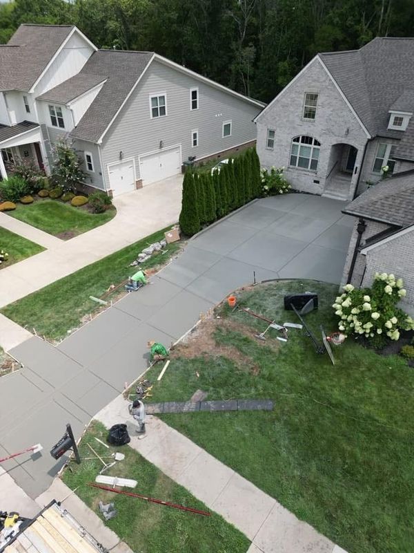 Driveway concrete work in progress. Houses and grass surround the new concrete. People working on the surface.