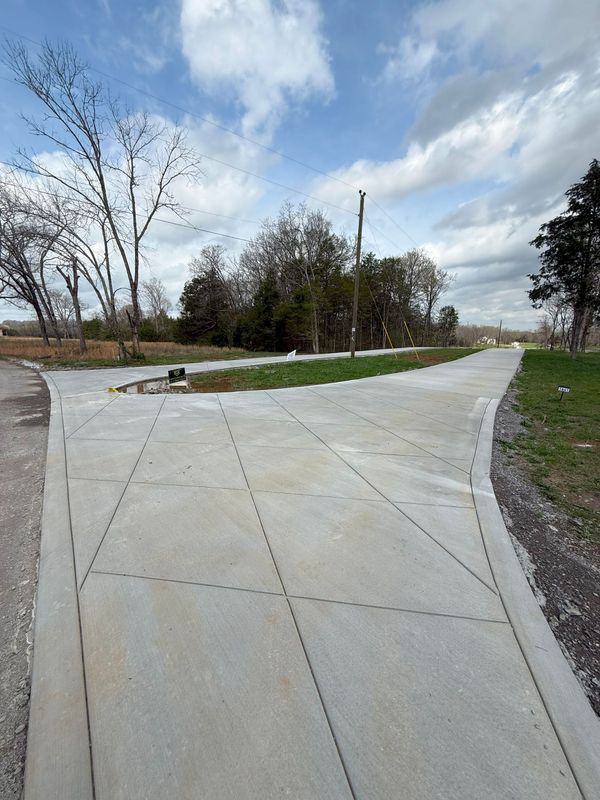 Concrete driveway forks into two directions, leading to a street under a cloudy sky.