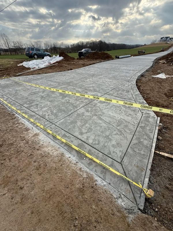 Newly poured concrete driveway with decorative pattern, caution tape, and vehicles in the distance.