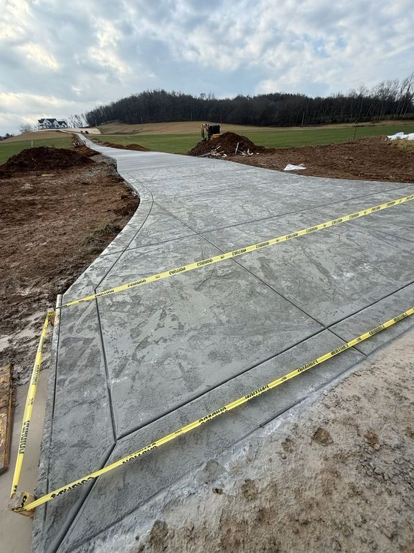 Newly poured concrete driveway with yellow caution tape, leading uphill toward a house.