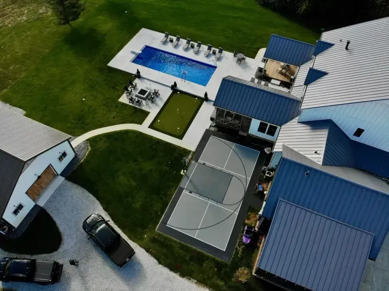 Aerial view of a modern home with a pool, sports court, and putting green on a large green lawn.