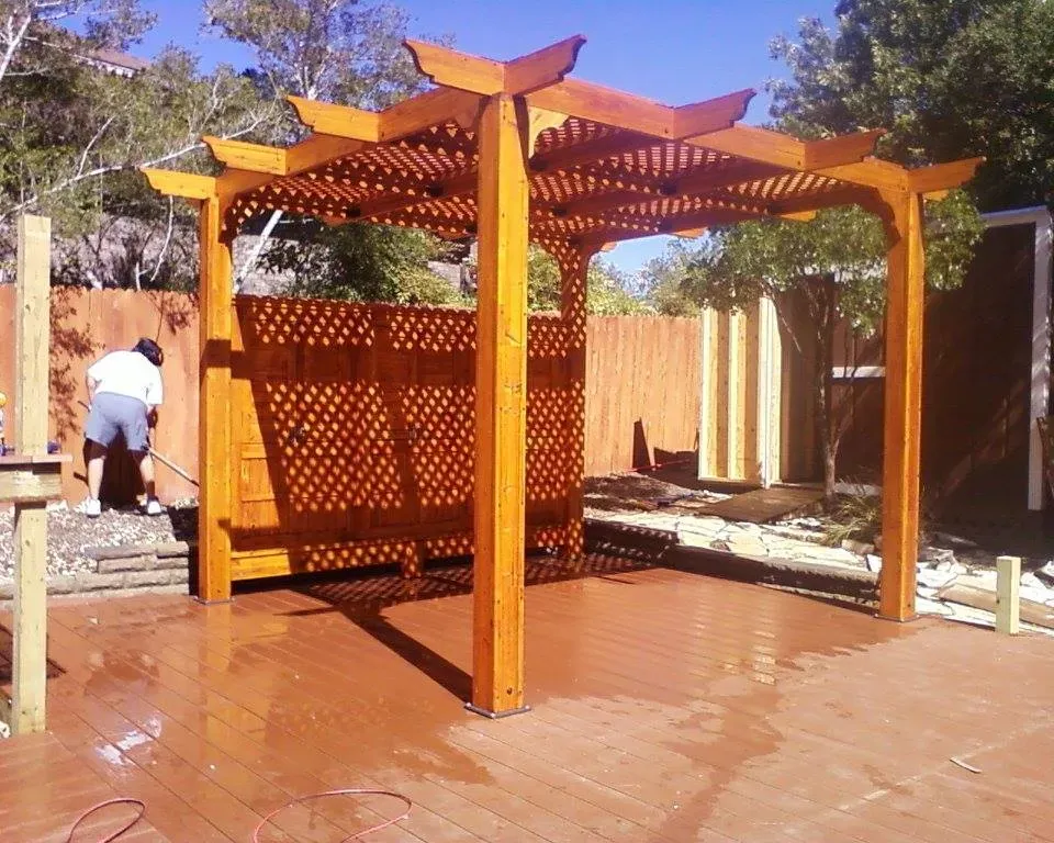 A man is standing under a wooden pergola in a backyard