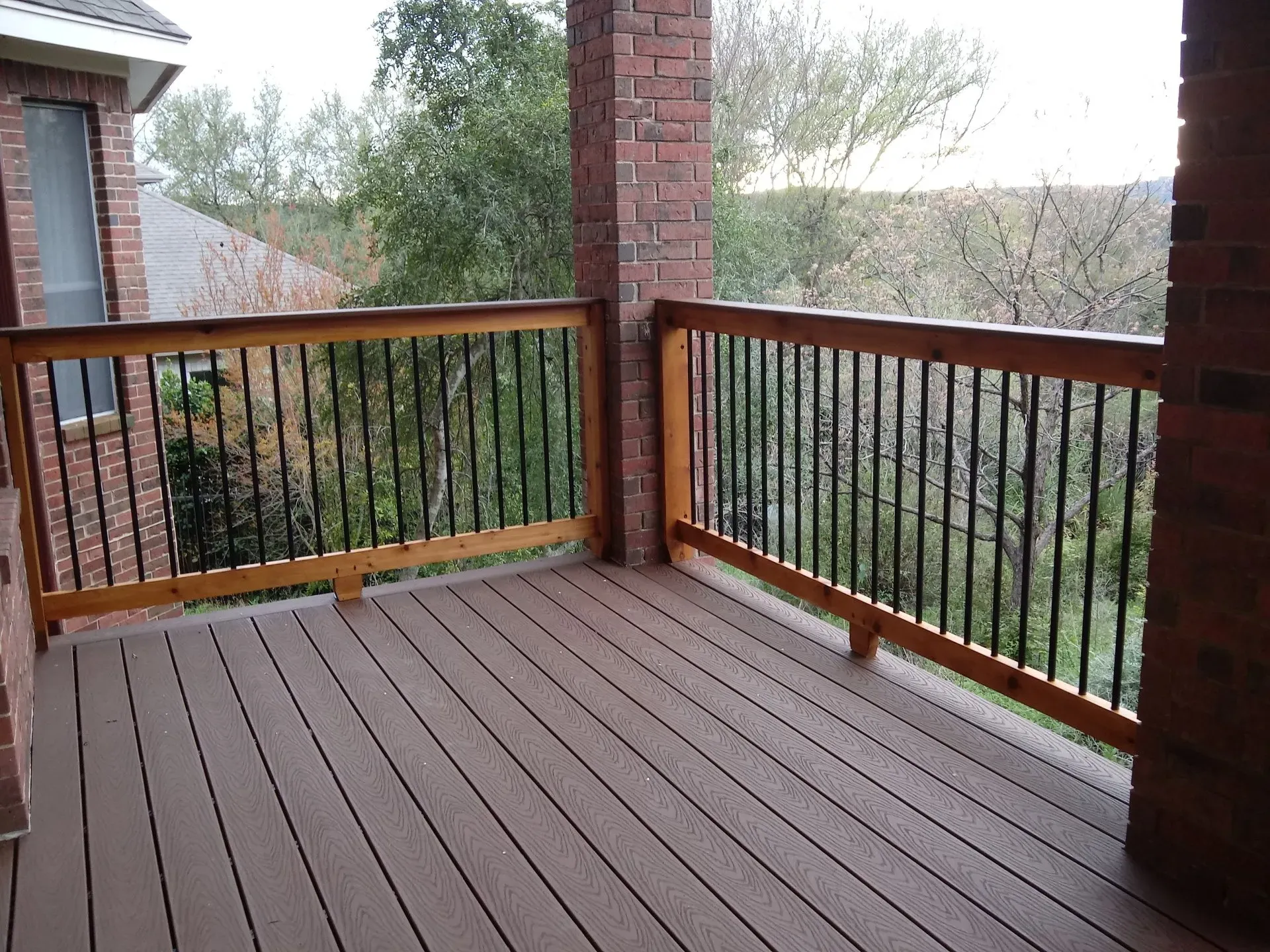 An empty deck with a wooden railing and a brick building in the background