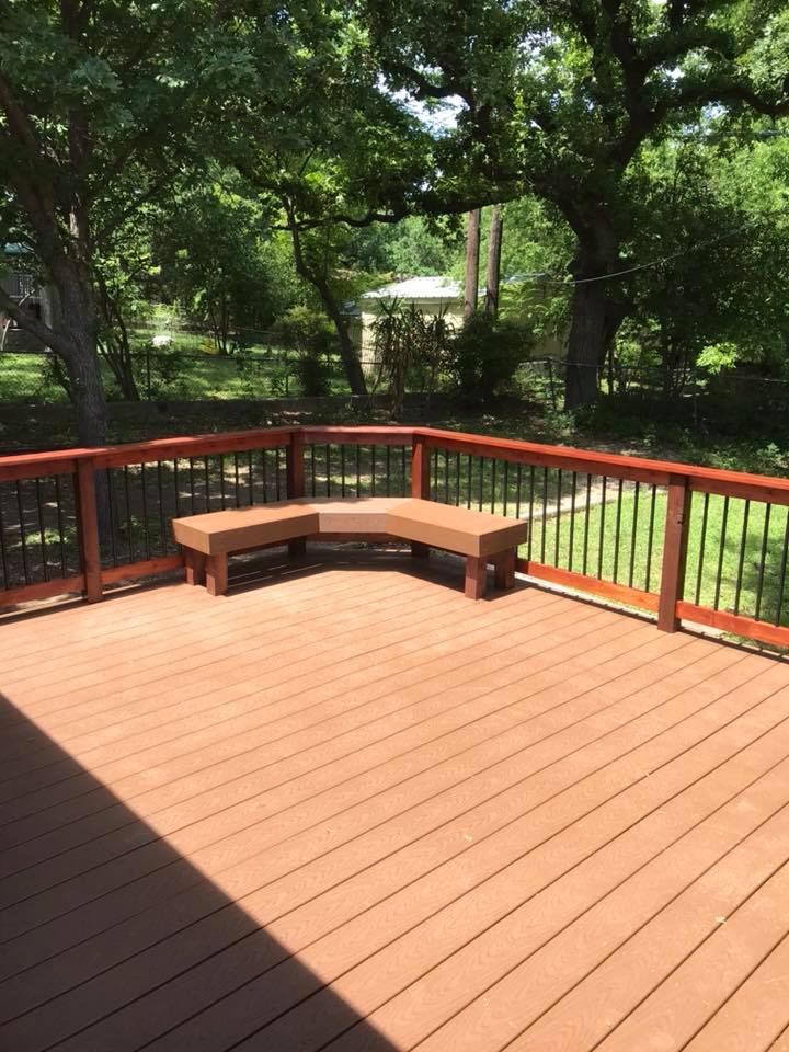 A wooden deck with a bench on it and trees in the background.