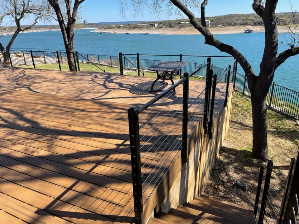 A wooden deck with a fence and a picnic table overlooking a lake.