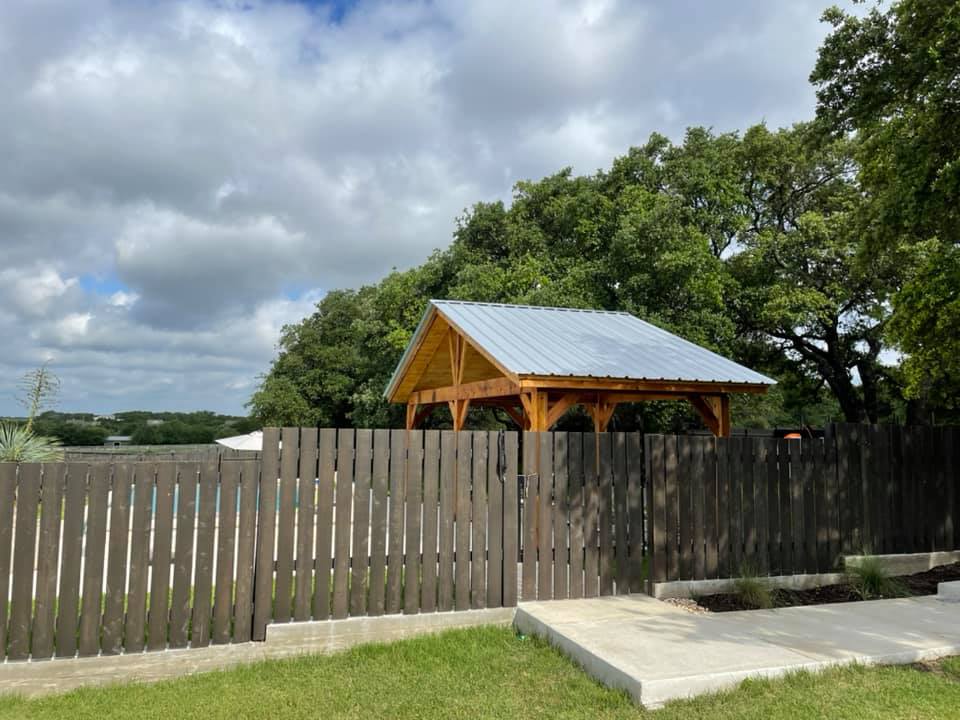 A wooden gazebo with a metal roof is behind a wooden fence.