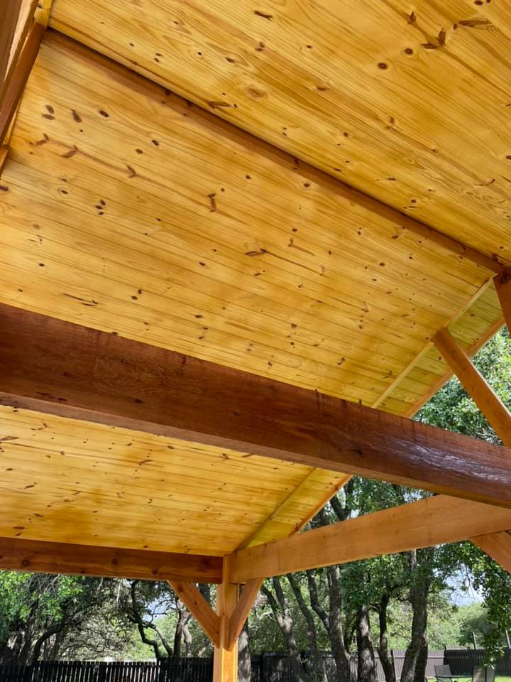 The ceiling of a wooden structure with trees in the background.