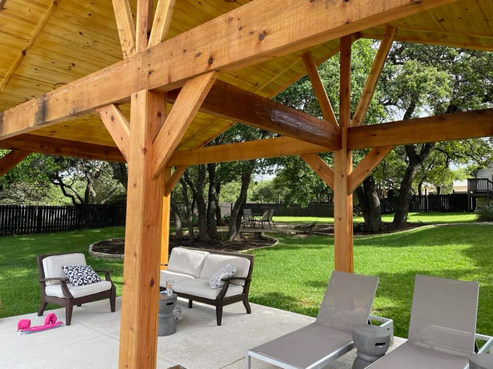 A wooden gazebo with a couch and chairs underneath it