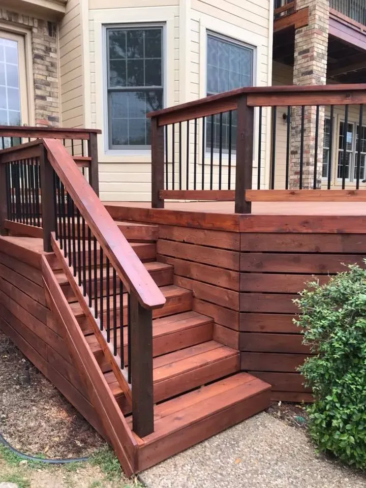 A wooden deck with stairs leading up to it in front of a house.