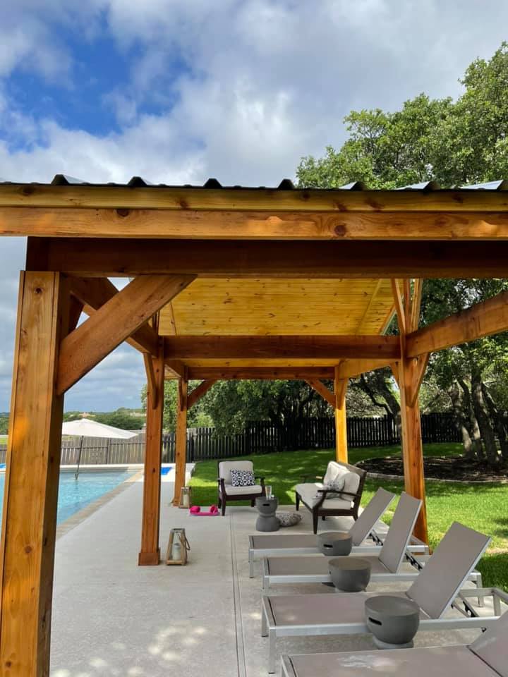 A row of lounge chairs under a wooden pergola next to a swimming pool