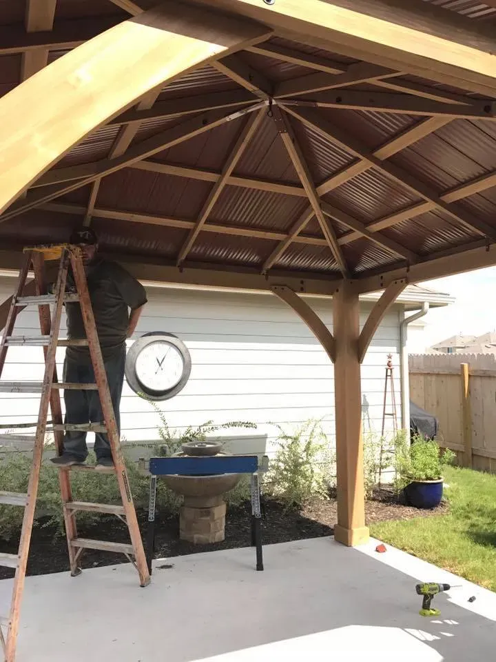 A man is standing on a ladder under a wooden gazebo.