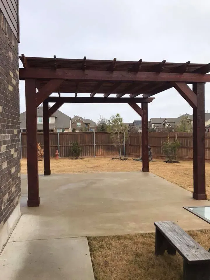 A wooden pergola is in the backyard of a house.