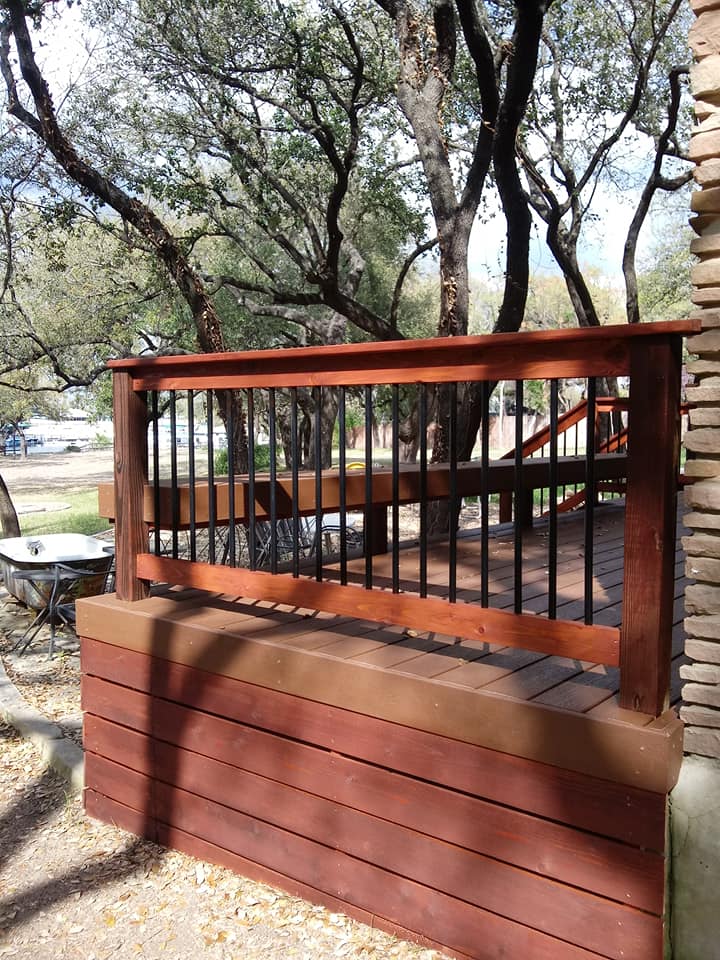 A wooden deck with a metal railing and trees in the background.