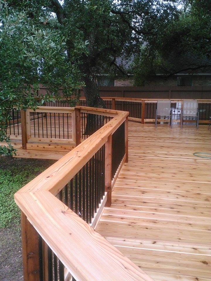 A wooden deck with a black railing and a tree in the background