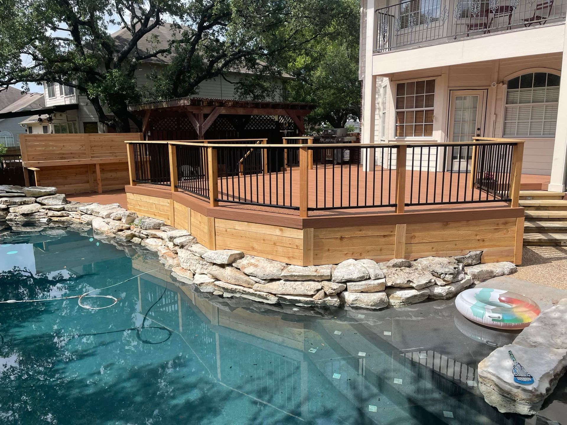 A large wooden deck is next to a swimming pool.