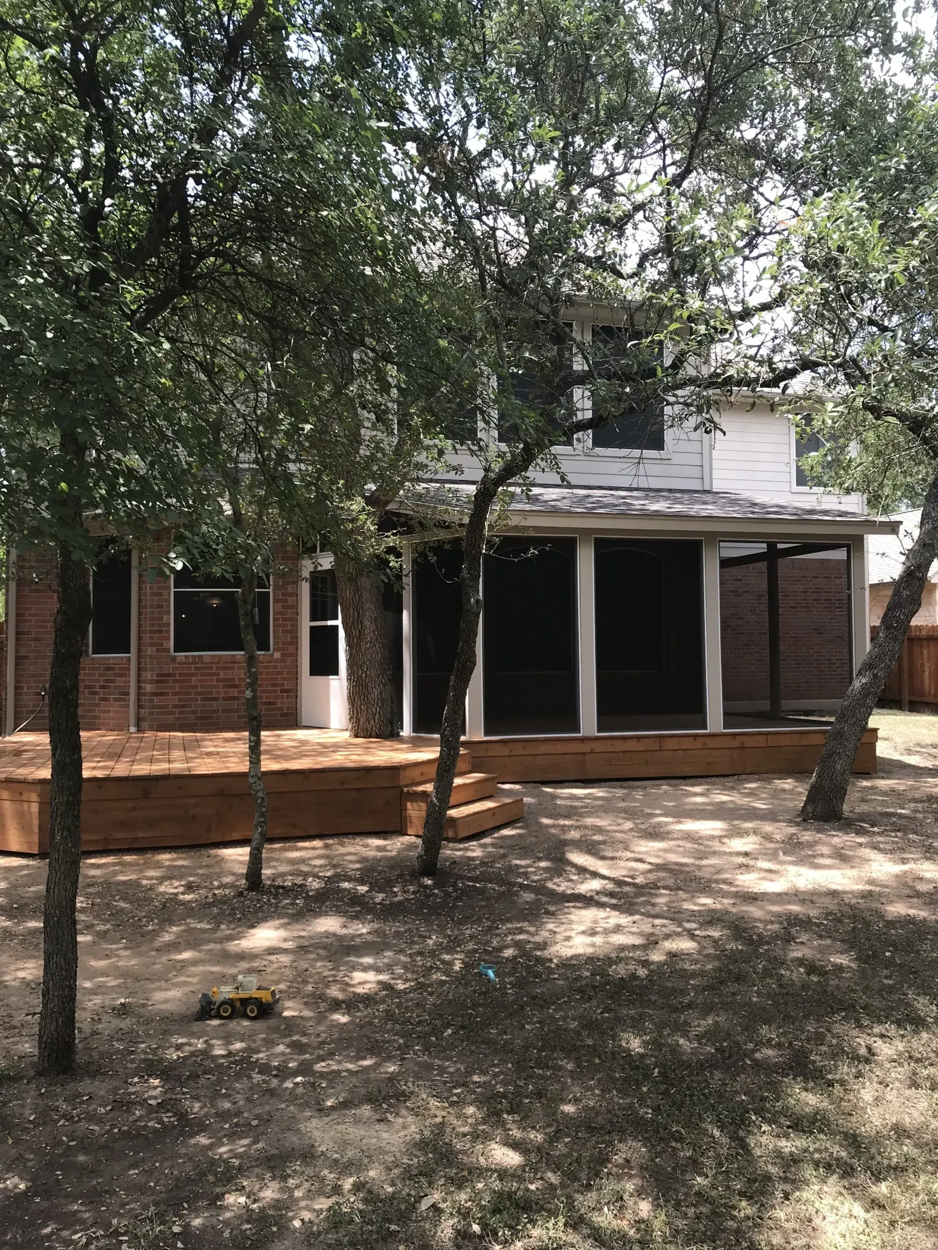A brick house with a wooden deck and a screened in porch surrounded by trees.