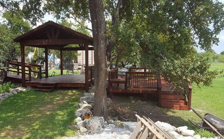 A wooden deck with a gazebo in the middle of a grassy field.