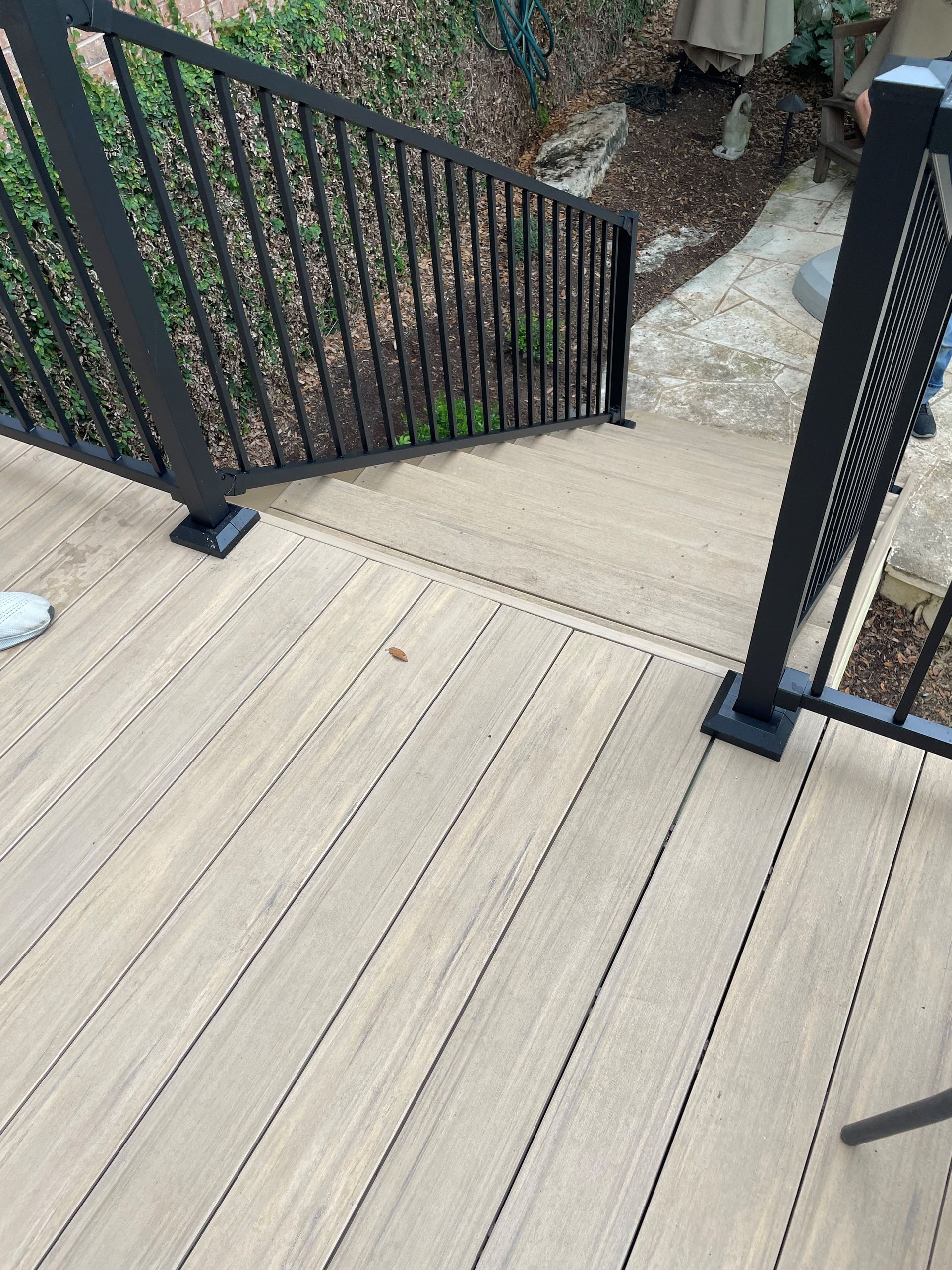A wooden deck with stairs leading up to it and a black railing.