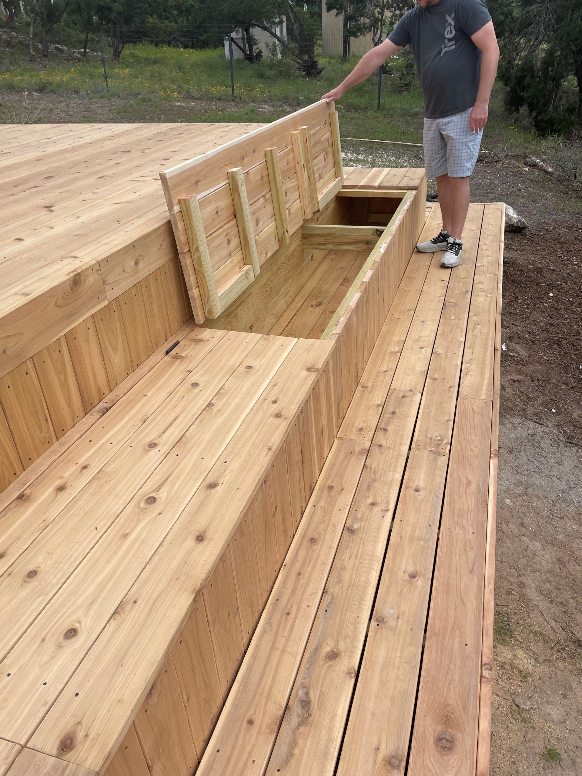 A man is standing on a wooden deck with a bench in the middle.