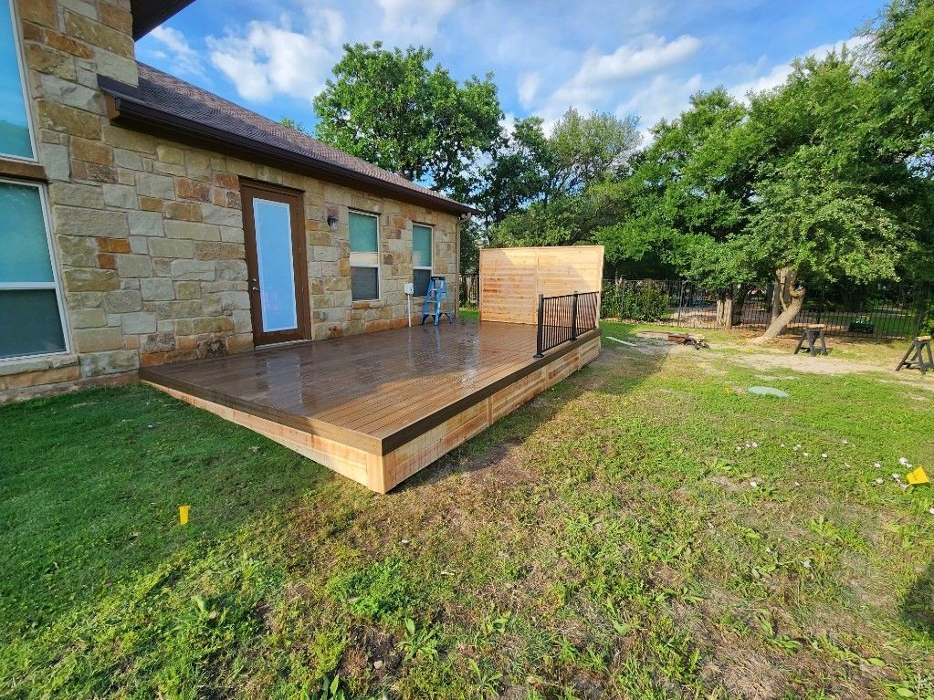 A wooden deck is sitting in the grass in front of a stone house.