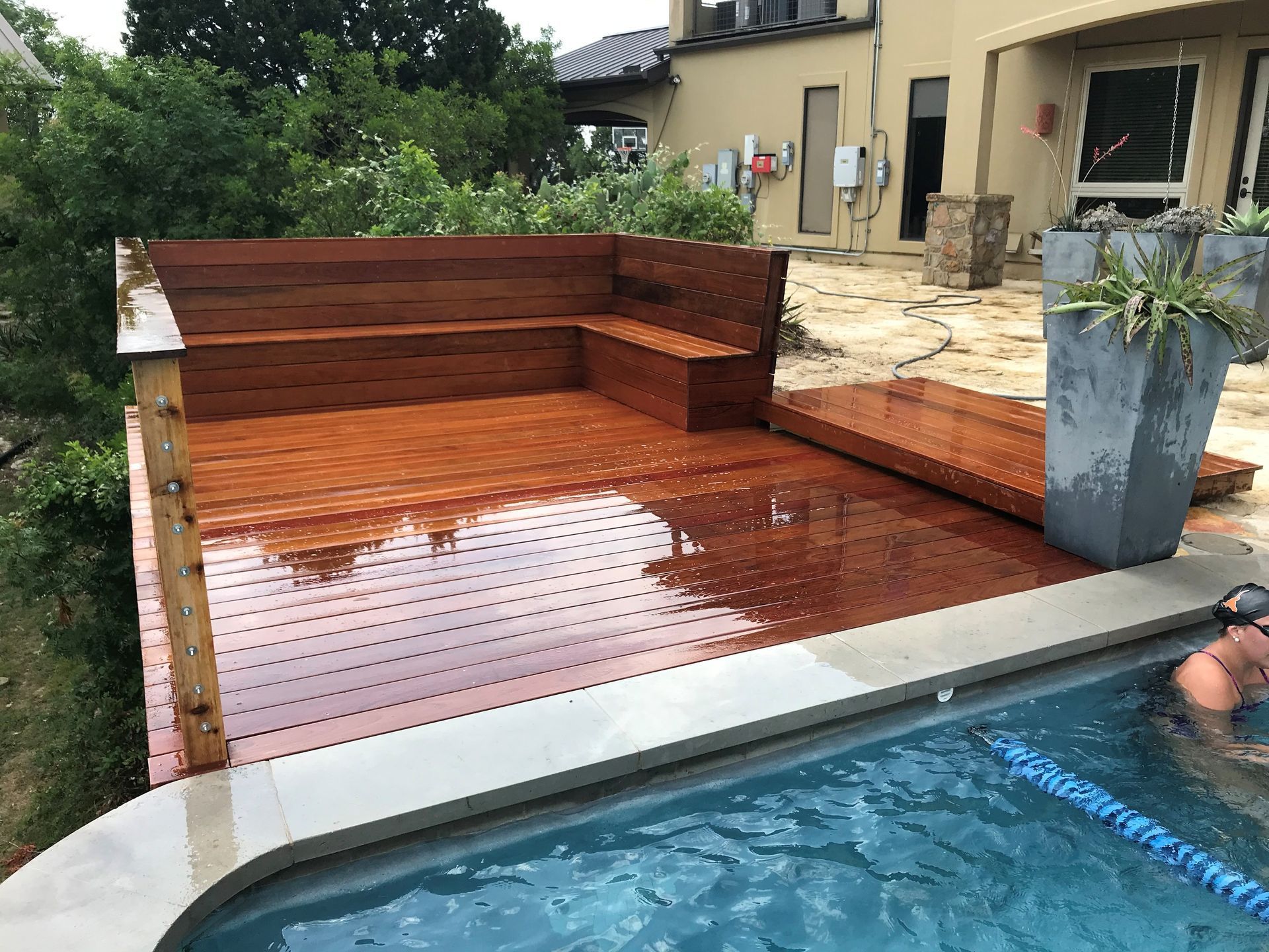 A person is swimming in a pool next to a wooden deck.