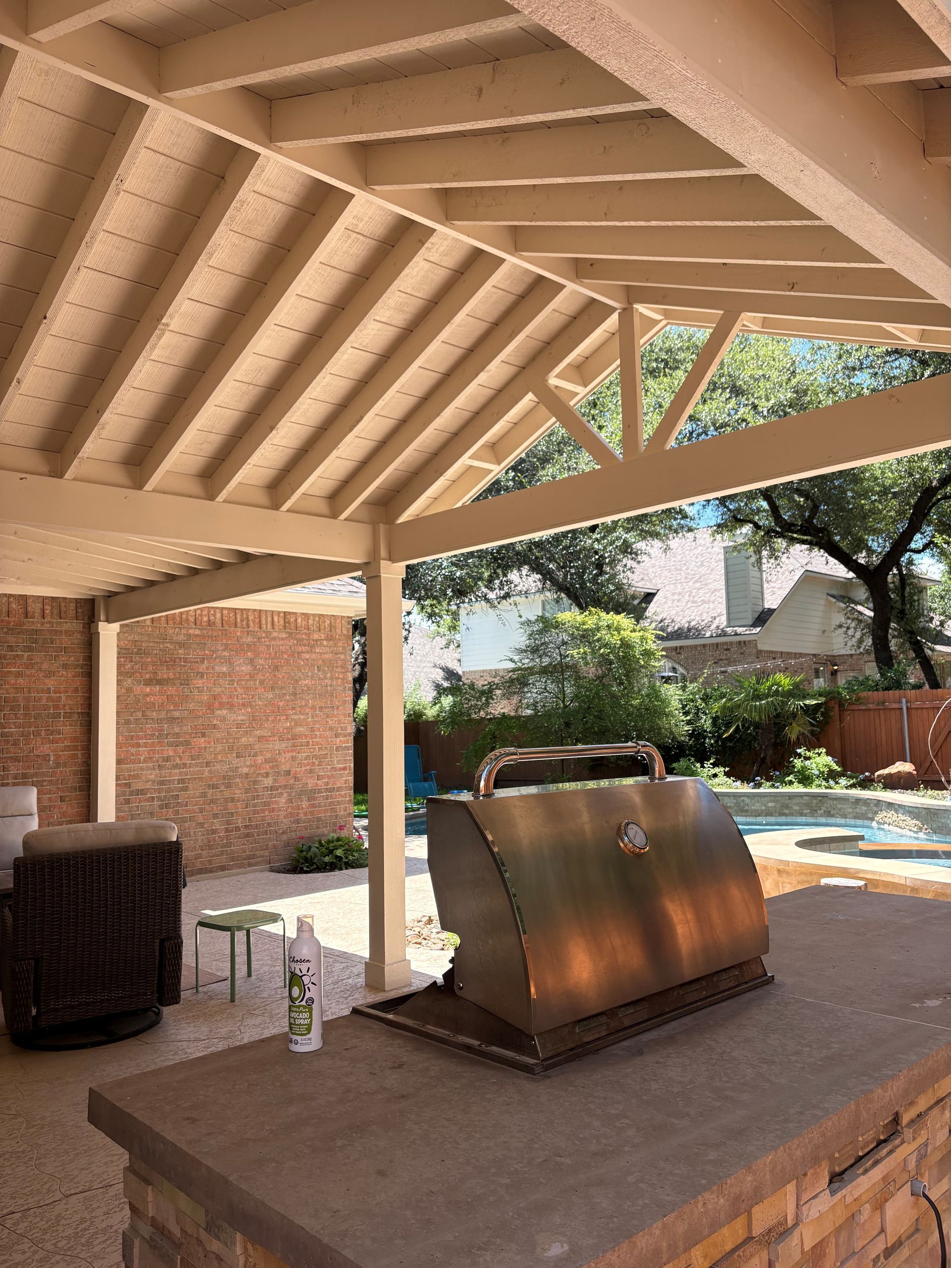 Covered backyard patio with a built-in grill and pool view