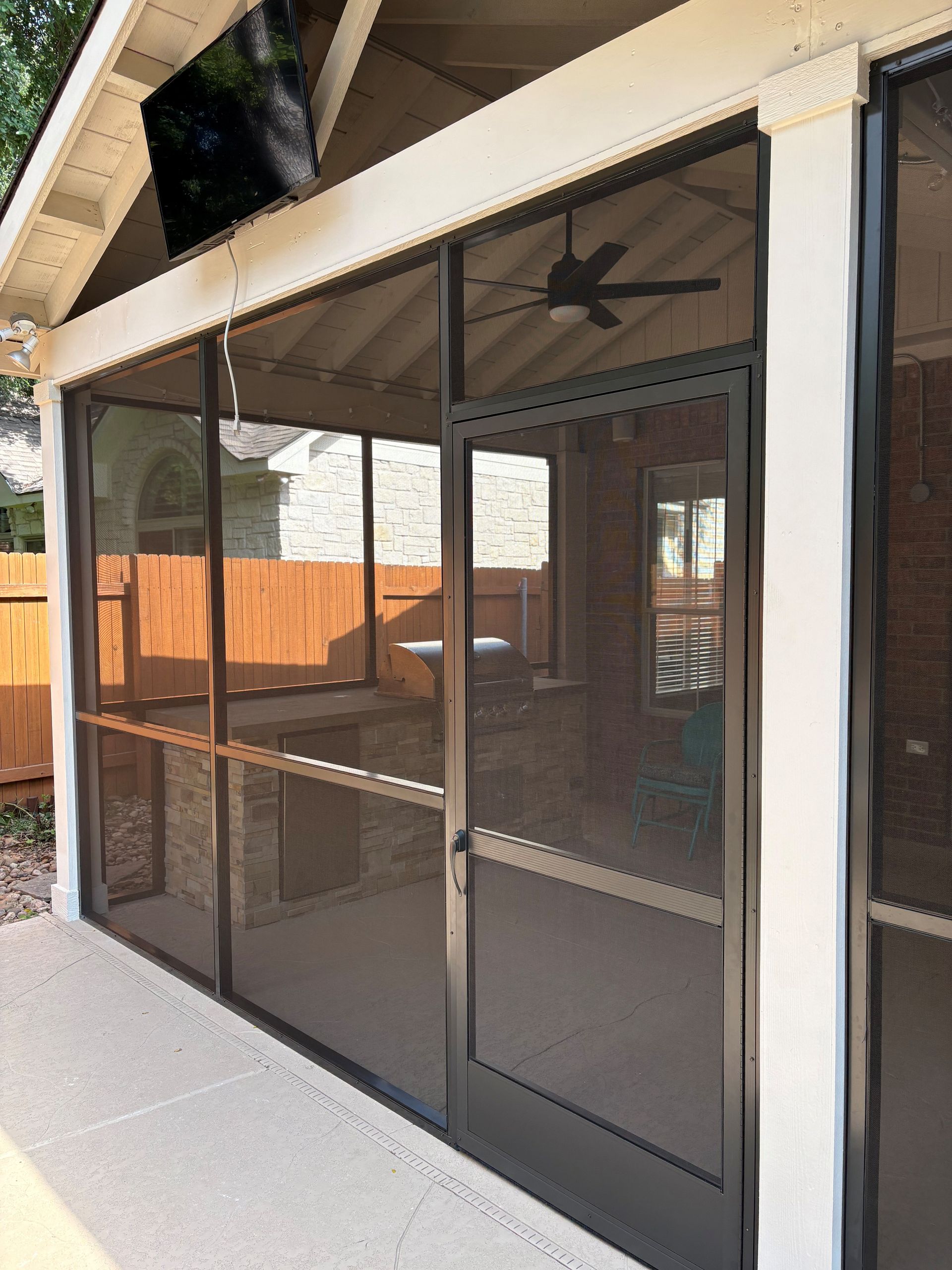 Screened patio enclosure with dark mesh doors and tan framing beside a house