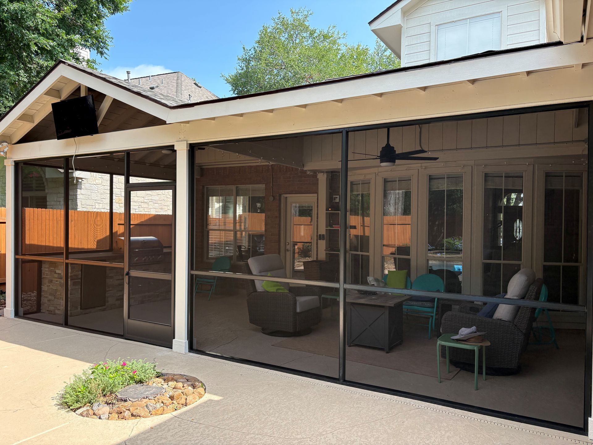 Covered patio with screened-in seating and a pergola beside a house, with potted plants and outdoor furniture.