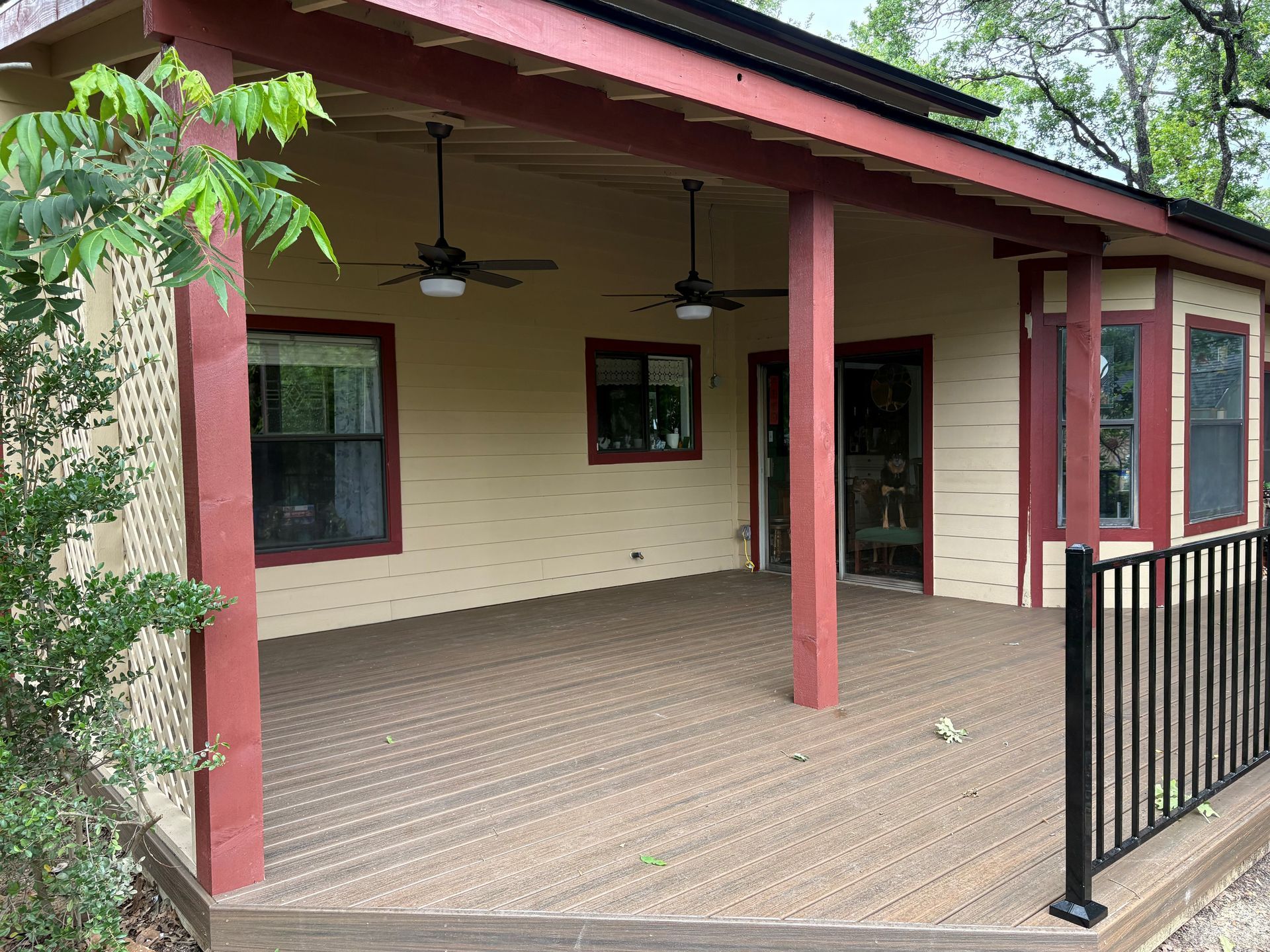 Covered porch with red posts, ceiling fans, and black railing on a cream house