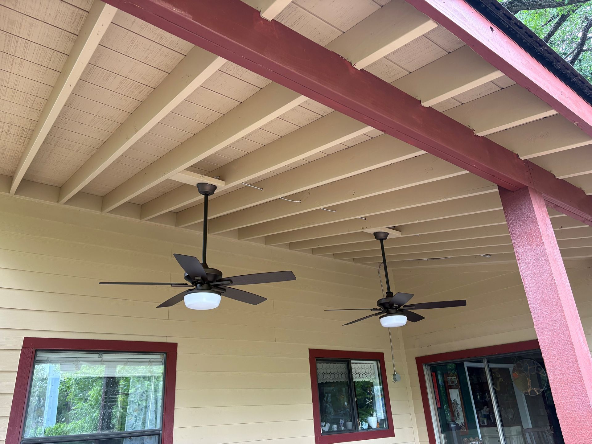 Covered porch with two ceiling fans, cream siding, red trim, and a sliding glass door