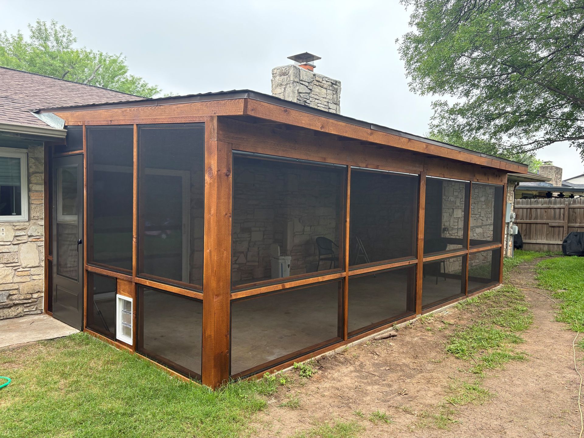 Screened porch with wooden beams attached to a stone house in a backyard
