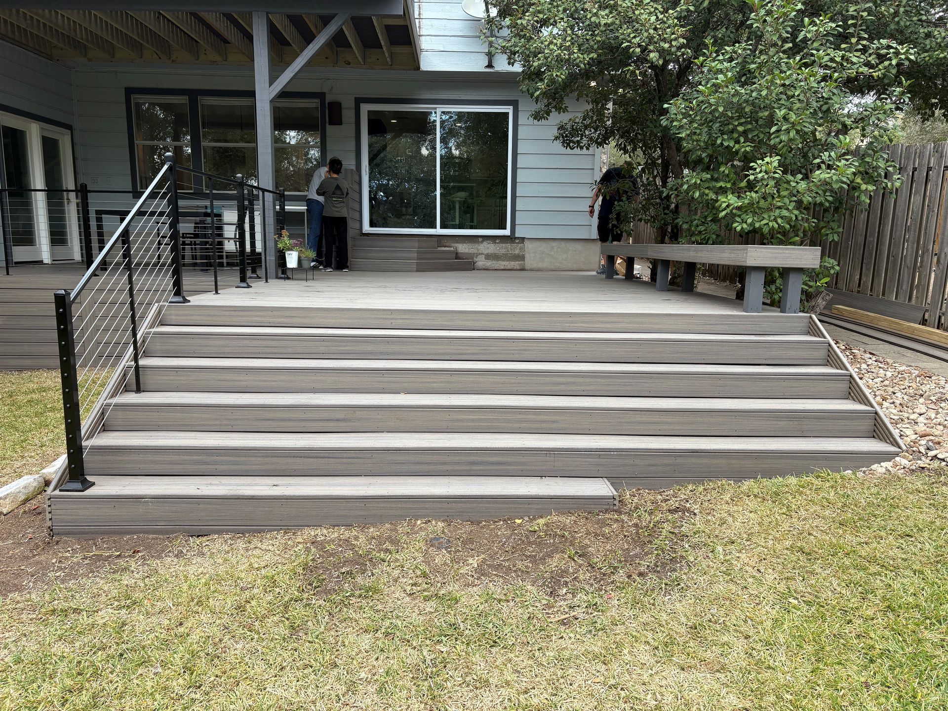 Front porch with wide steps, black handrails, and a person standing by the entrance of a house.