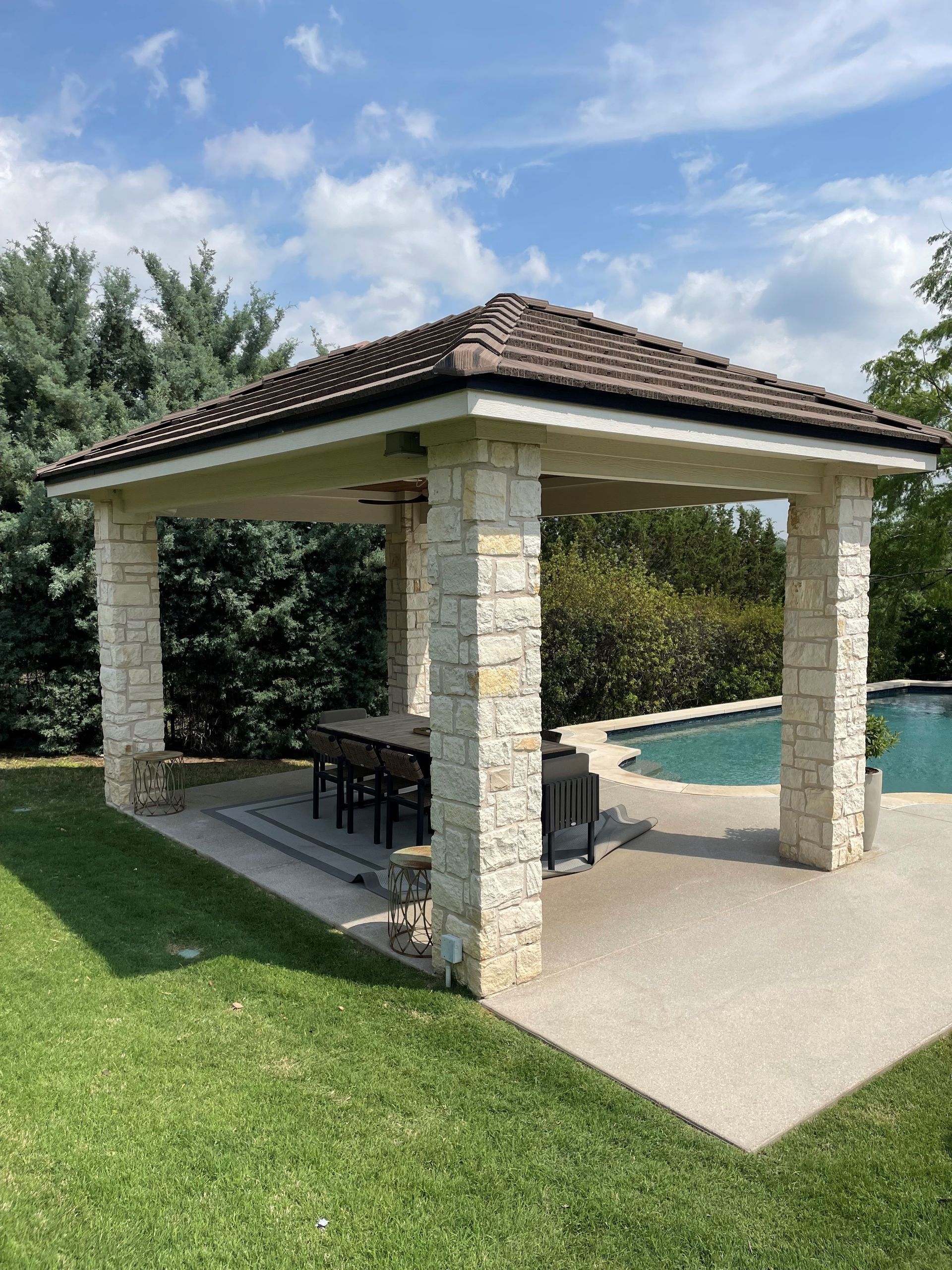 A gazebo with a table and chairs in front of a pool.