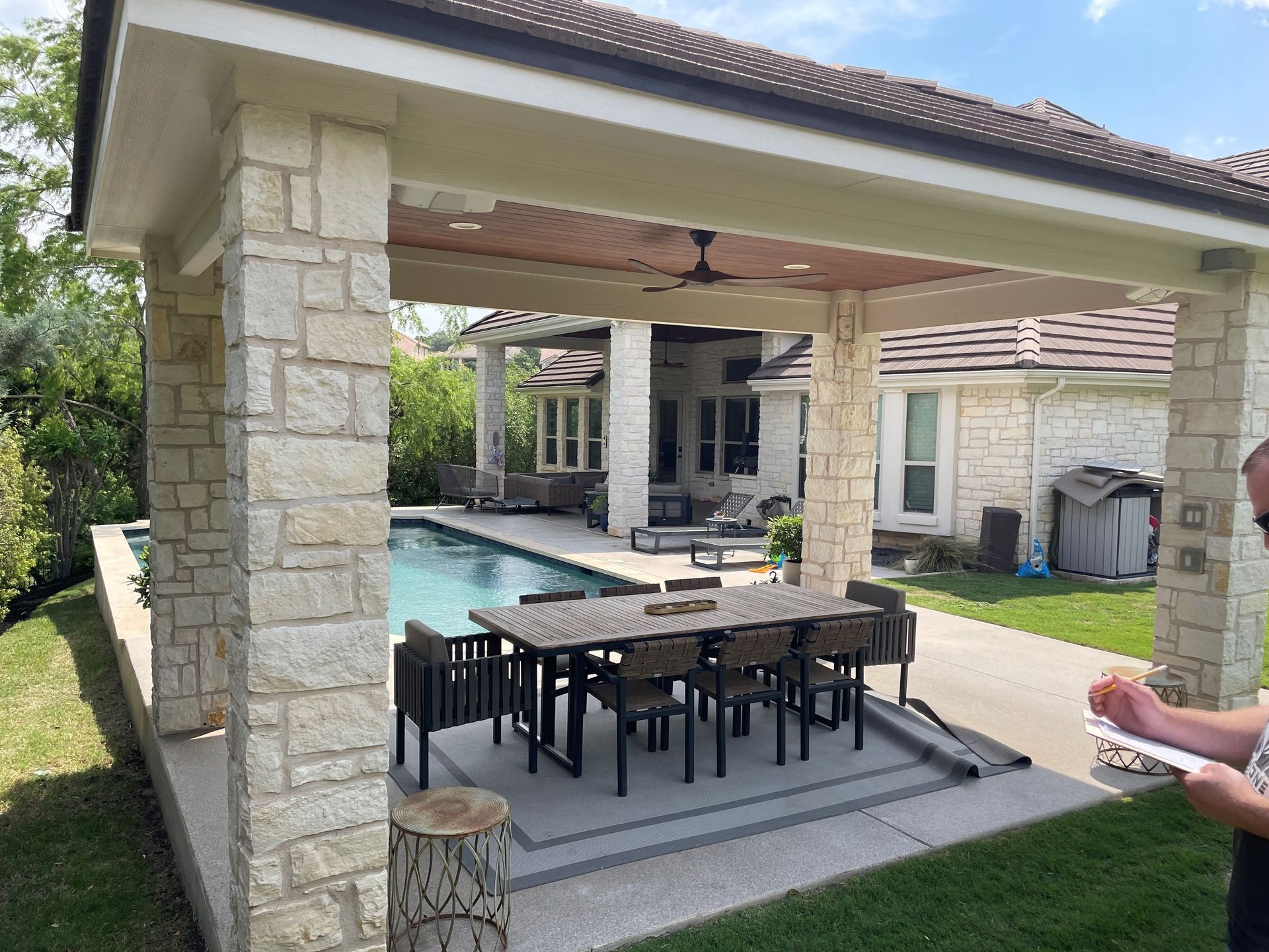 A man is standing in front of a patio with a table and chairs and a pool.