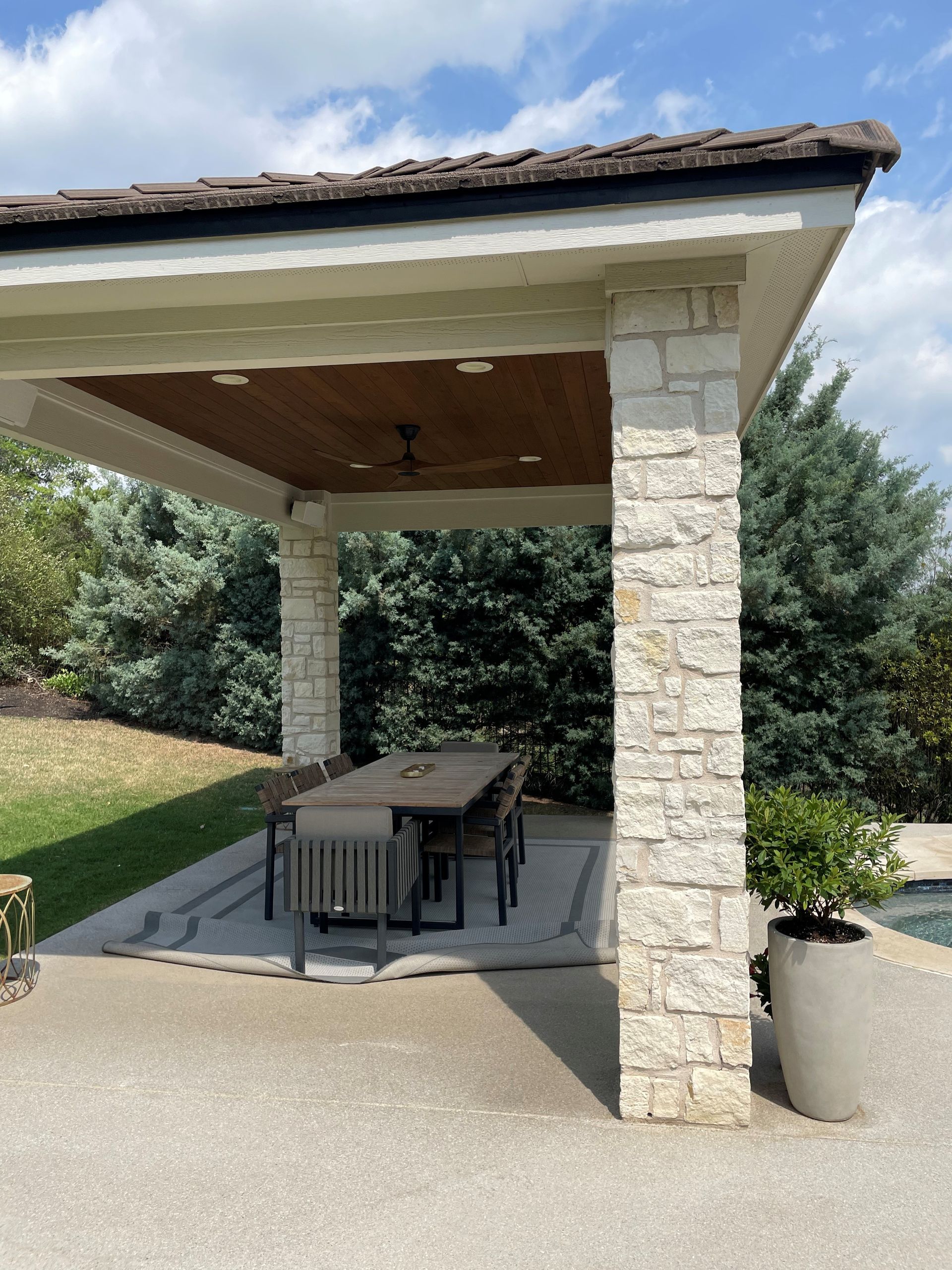 Stone patio pavilion with wooden ceiling and dining table in a landscaped outdoor area