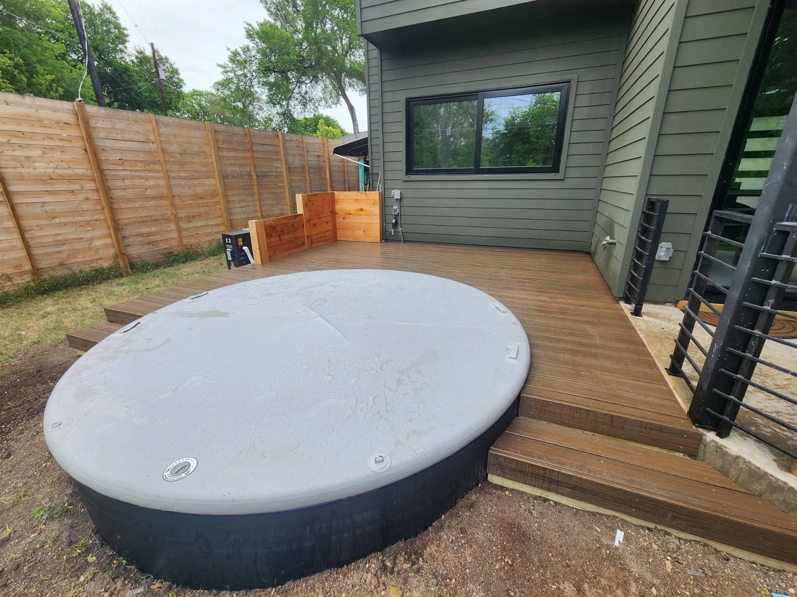 A round hot tub is sitting on a wooden deck in the backyard of a house.