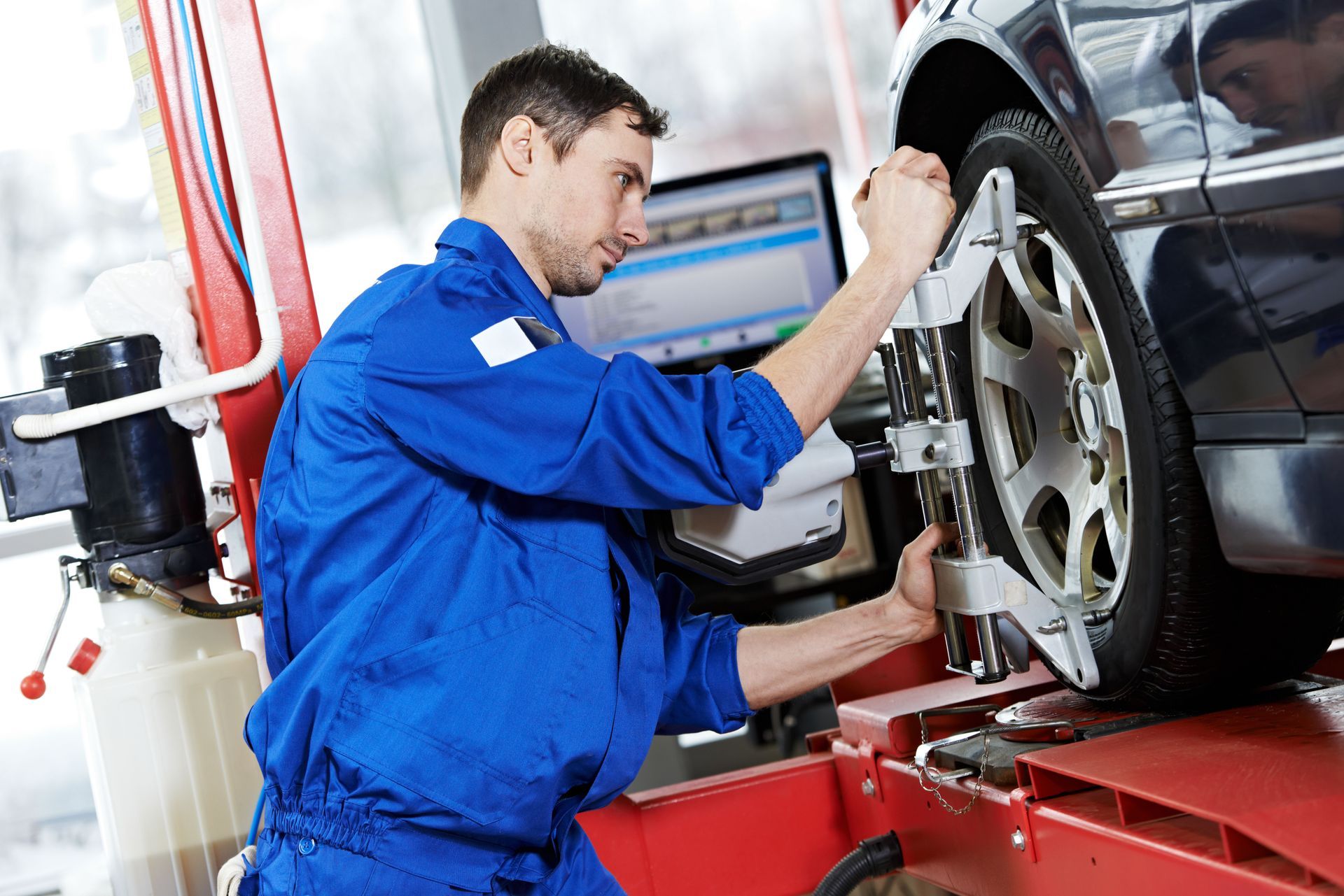 Mechanic in blue coveralls inspecting a car wheel on a red alignment machine