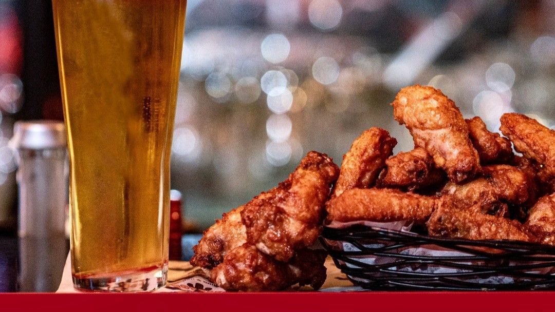 A tall glass of golden beer next to a basket of crispy, golden-brown fried chicken wings.