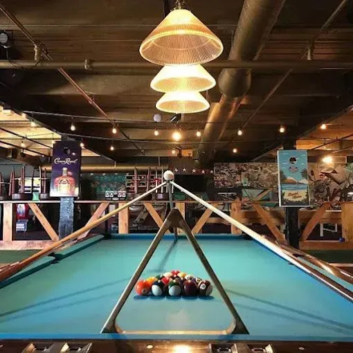 Pool table in a bar with balls racked, overhead lamps, and various decorations.
