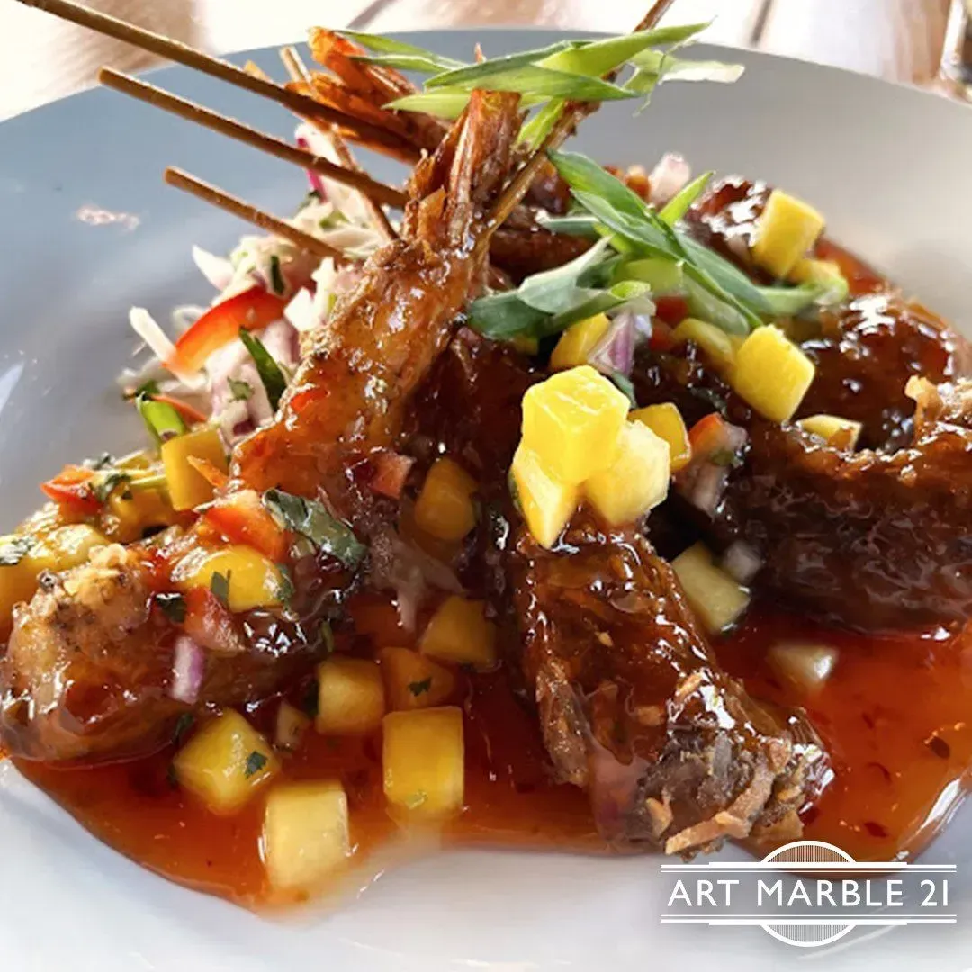 Shrimp skewers with mango salsa and sauce on a white plate. Garnished with green onions.