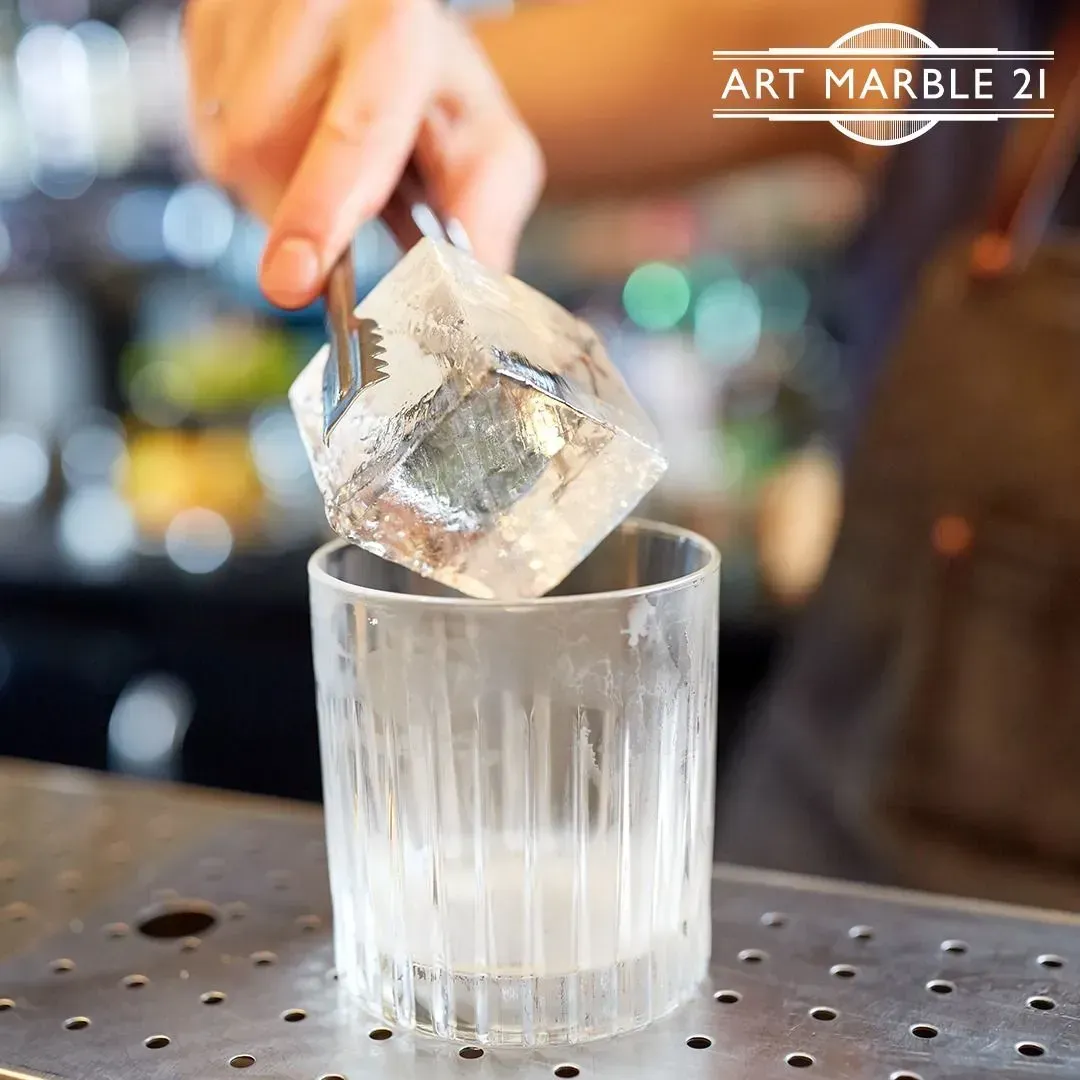 Bartender placing a large ice cube in a ribbed glass.