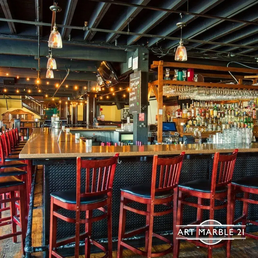 Bar with red stools, wooden counter, and bottles displayed behind the bar, lit by string lights.