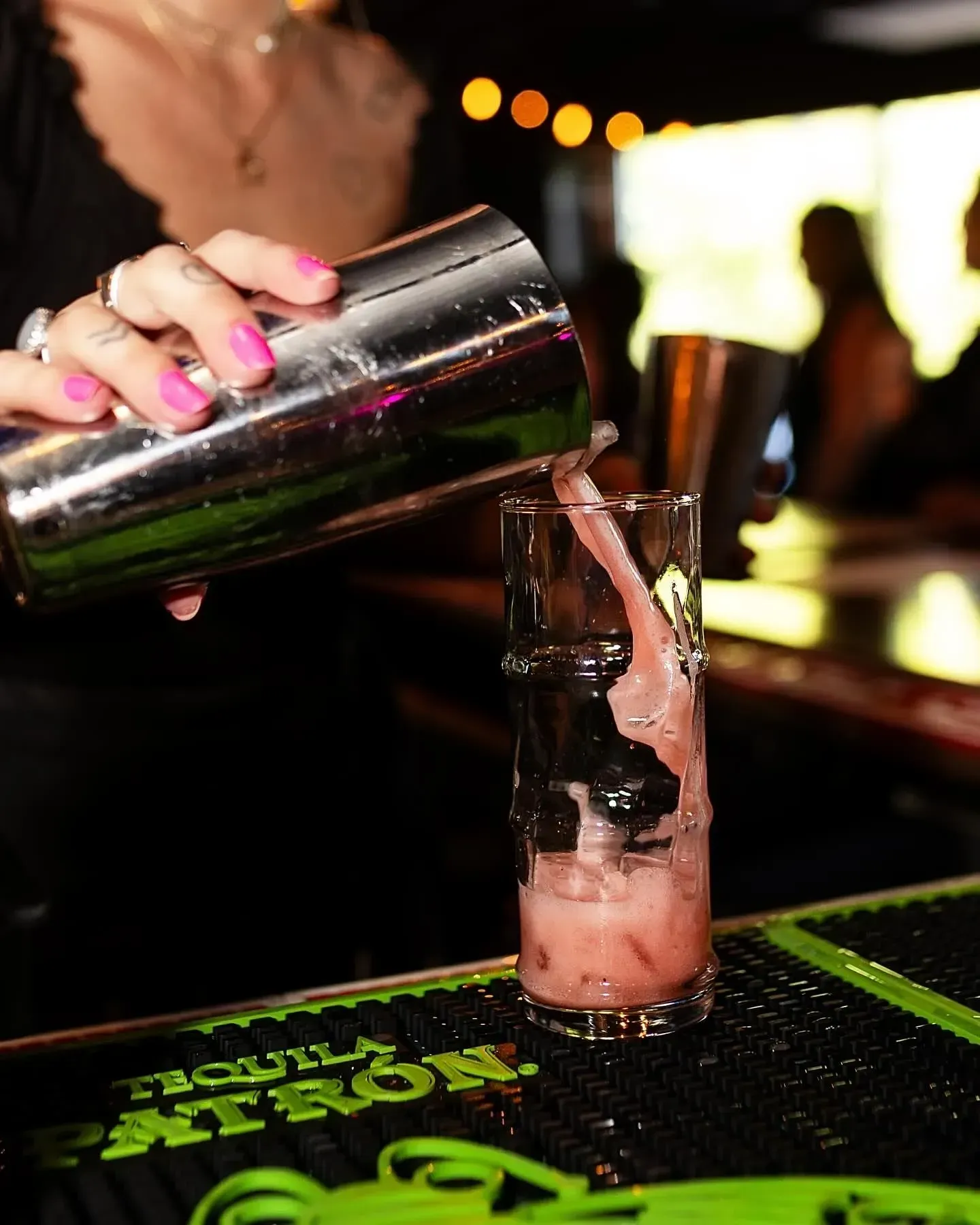 Bartender pouring a pink cocktail from a shaker into a glass with ice.