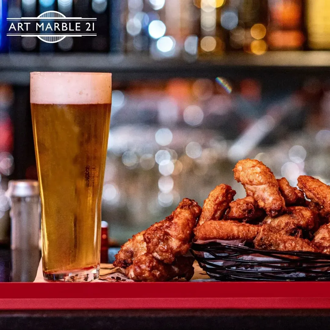 Glass of beer and basket of fried chicken wings on a bar.