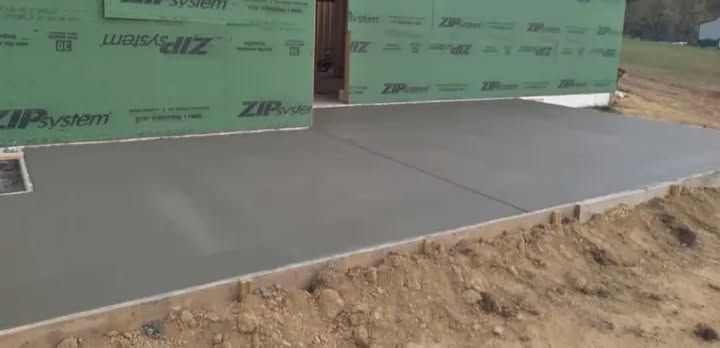 Concrete slab at a construction site beside green house-wrap and exposed dirt