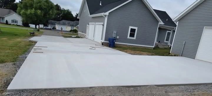 Freshly poured concrete driveway beside a gray house in a suburban neighborhood