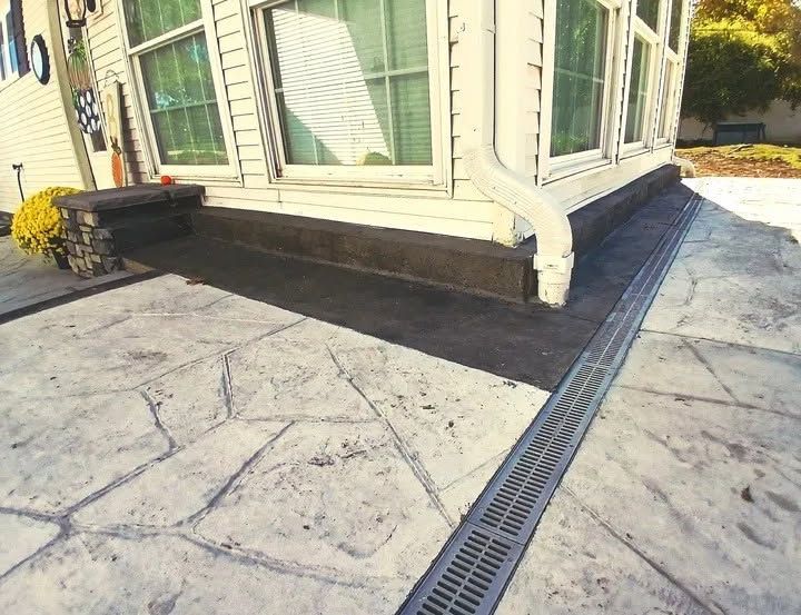 Exterior corner of a light-colored house with stamped concrete patio and a drainage grate