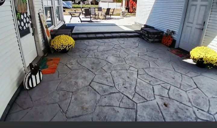 Stone-paver backyard patio with potted yellow flowers and outdoor seating in the distance