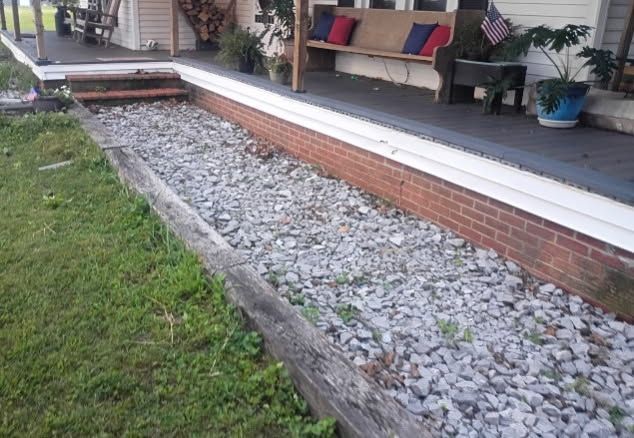 Rock garden beside a covered porch with red brick edging and benches with colorful cushions