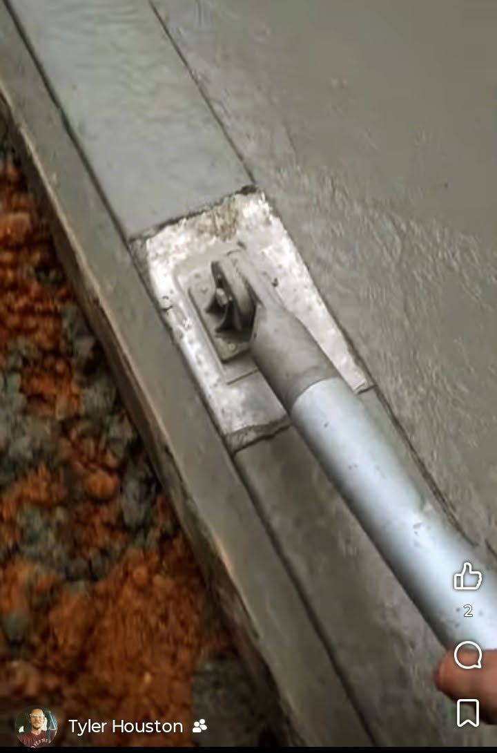 Close-up of a metal tool handle attached to a silver bracket on a gray surface beside carpet.